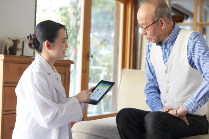 家庭を訪問し、健康状態についてタブレットに入力しているケースワーカー