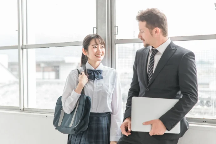 将来を見据える国際学部志望の女子高校生が英語教師と廊下で話す様子